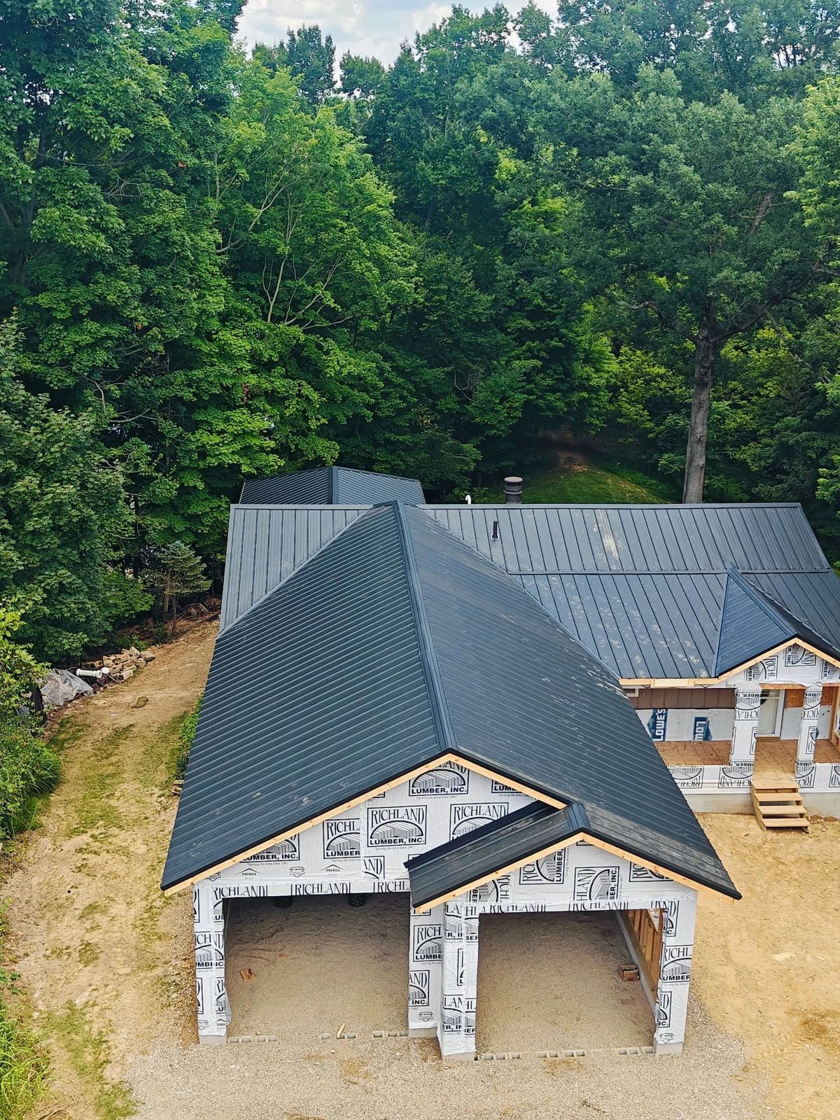 Garage and house under construction with black roofing, surrounded by trees.