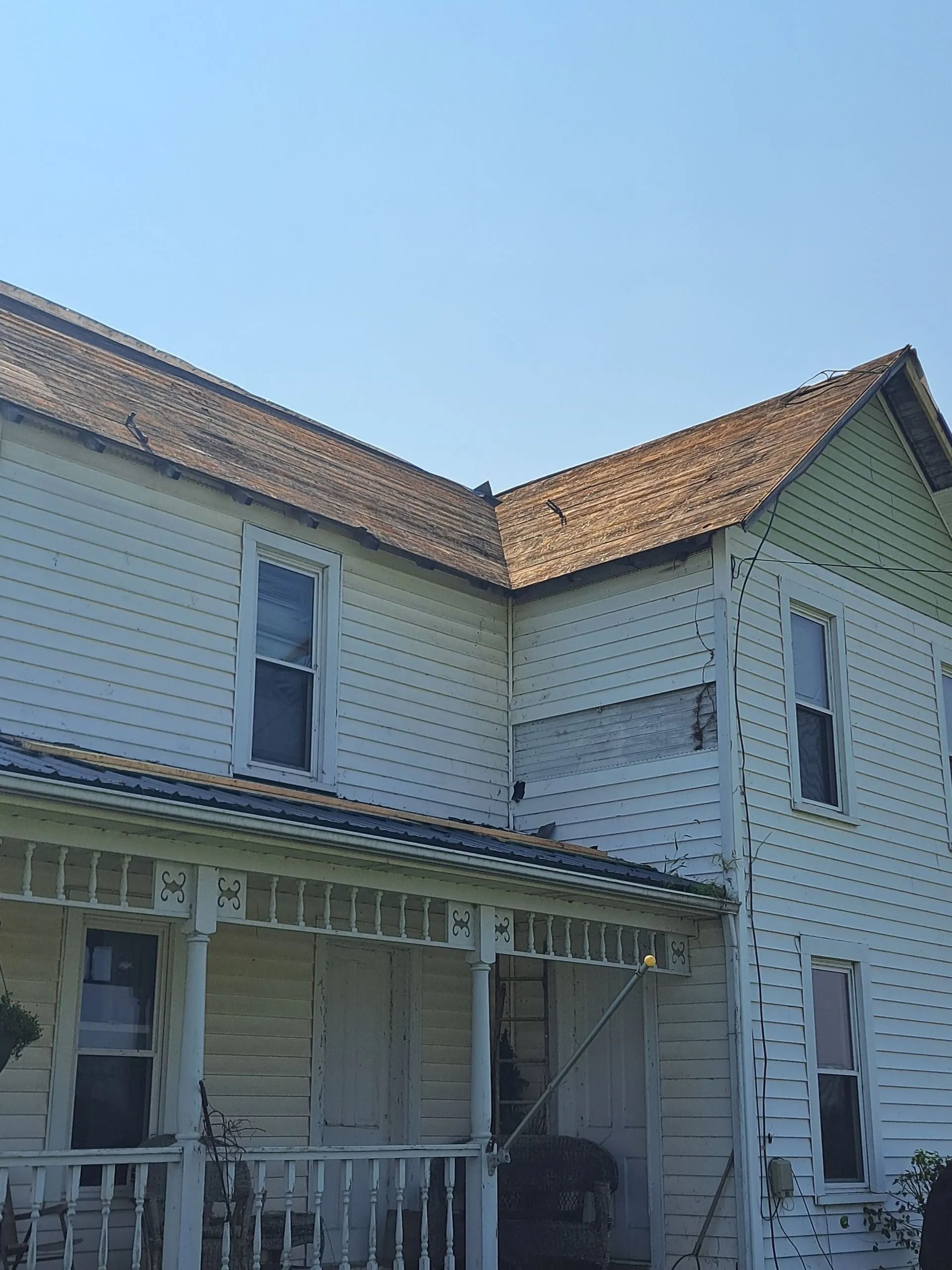 Two-story white house with a weathered brown roof and porch, under a clear blue sky.