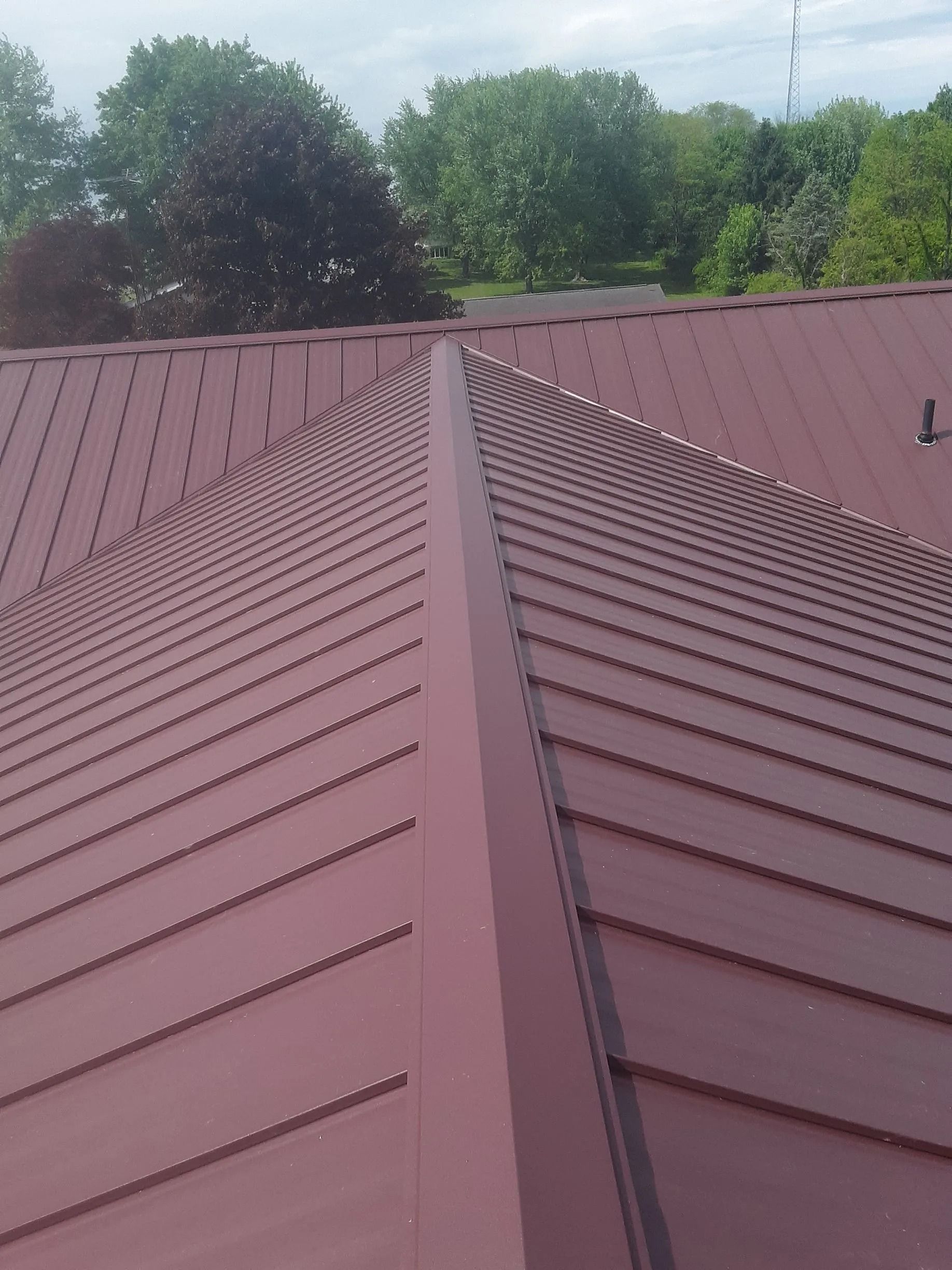 Red metal roof with a central ridge, set against a backdrop of trees and a cloudy sky.