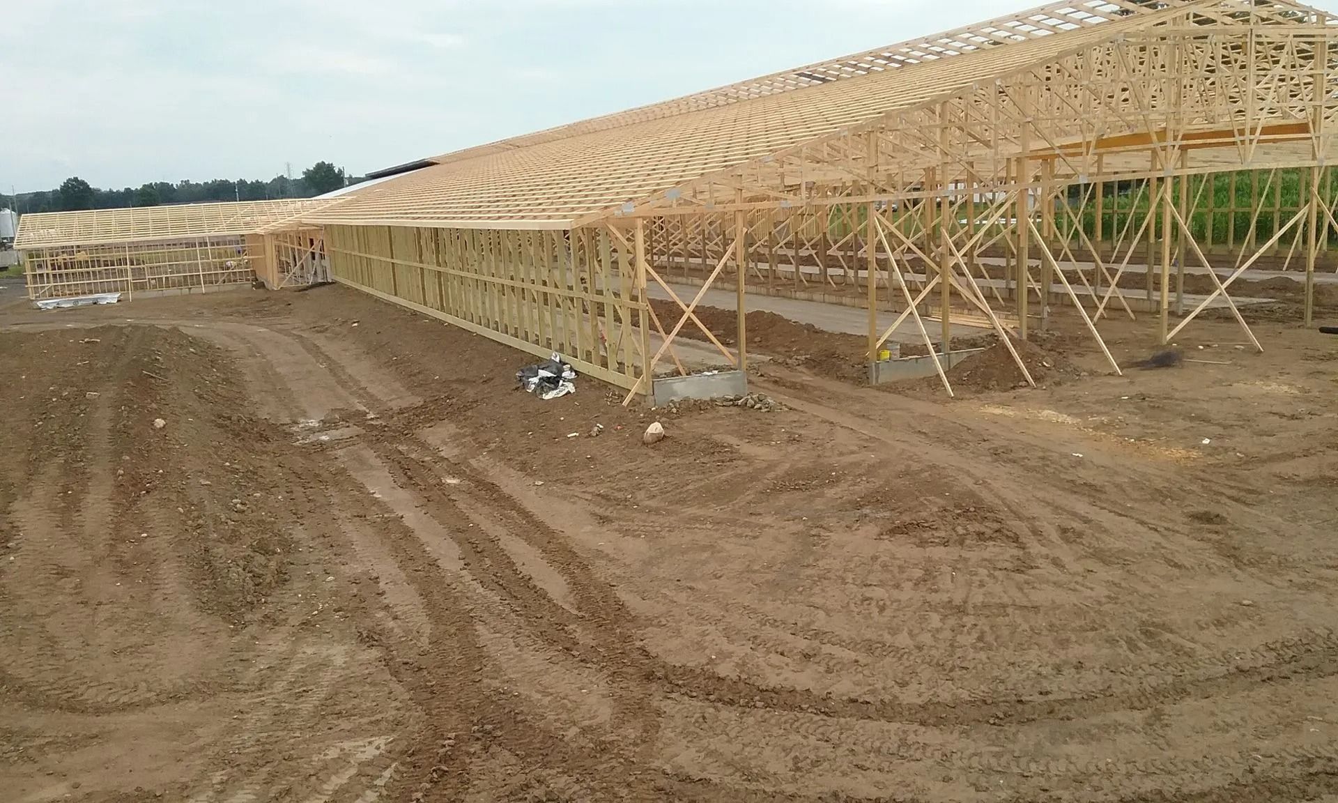 Wooden structure under construction in a muddy field, with a partially built roof.