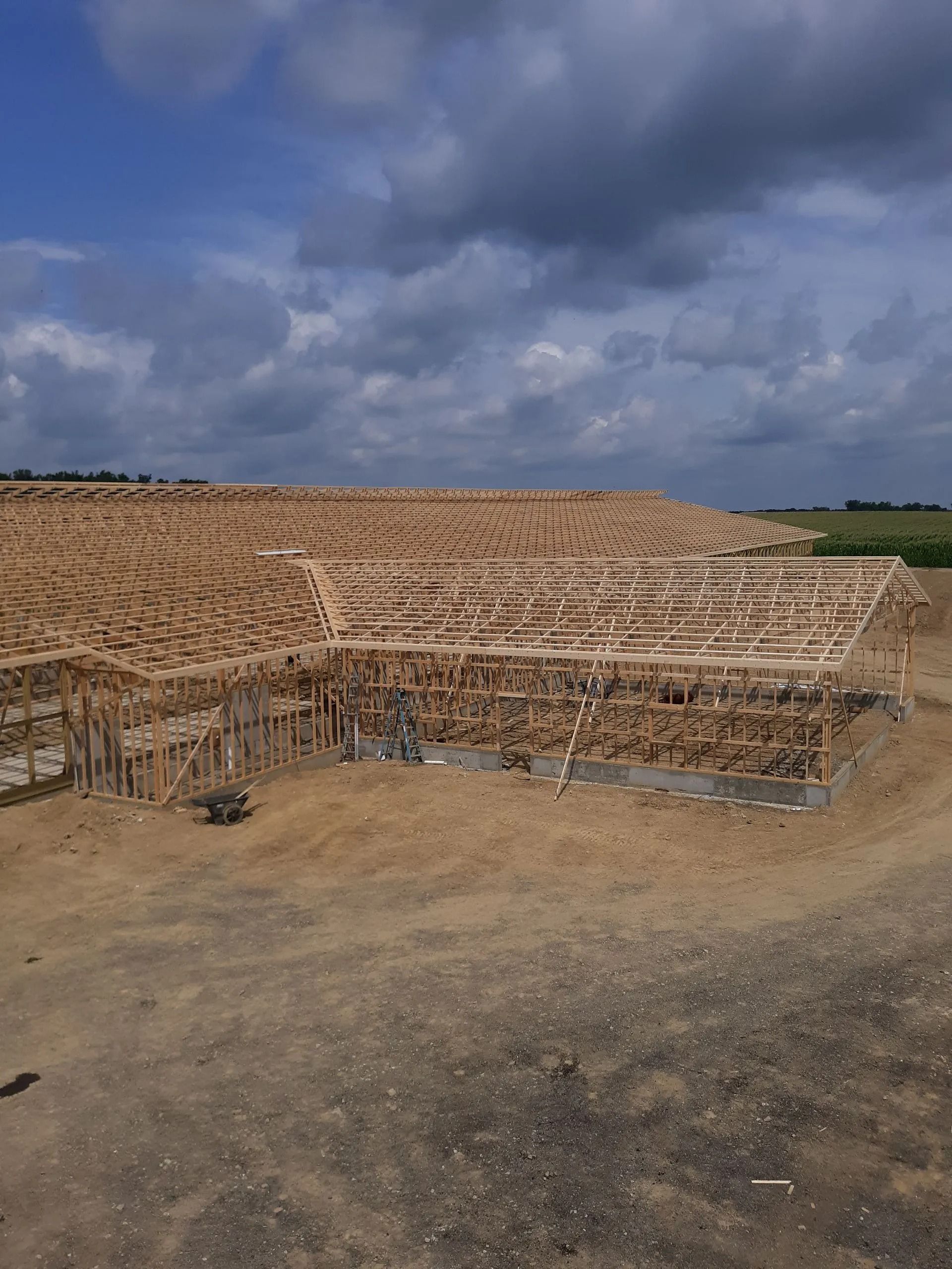 Construction site with wooden structures and earthworks, under a cloudy blue sky.