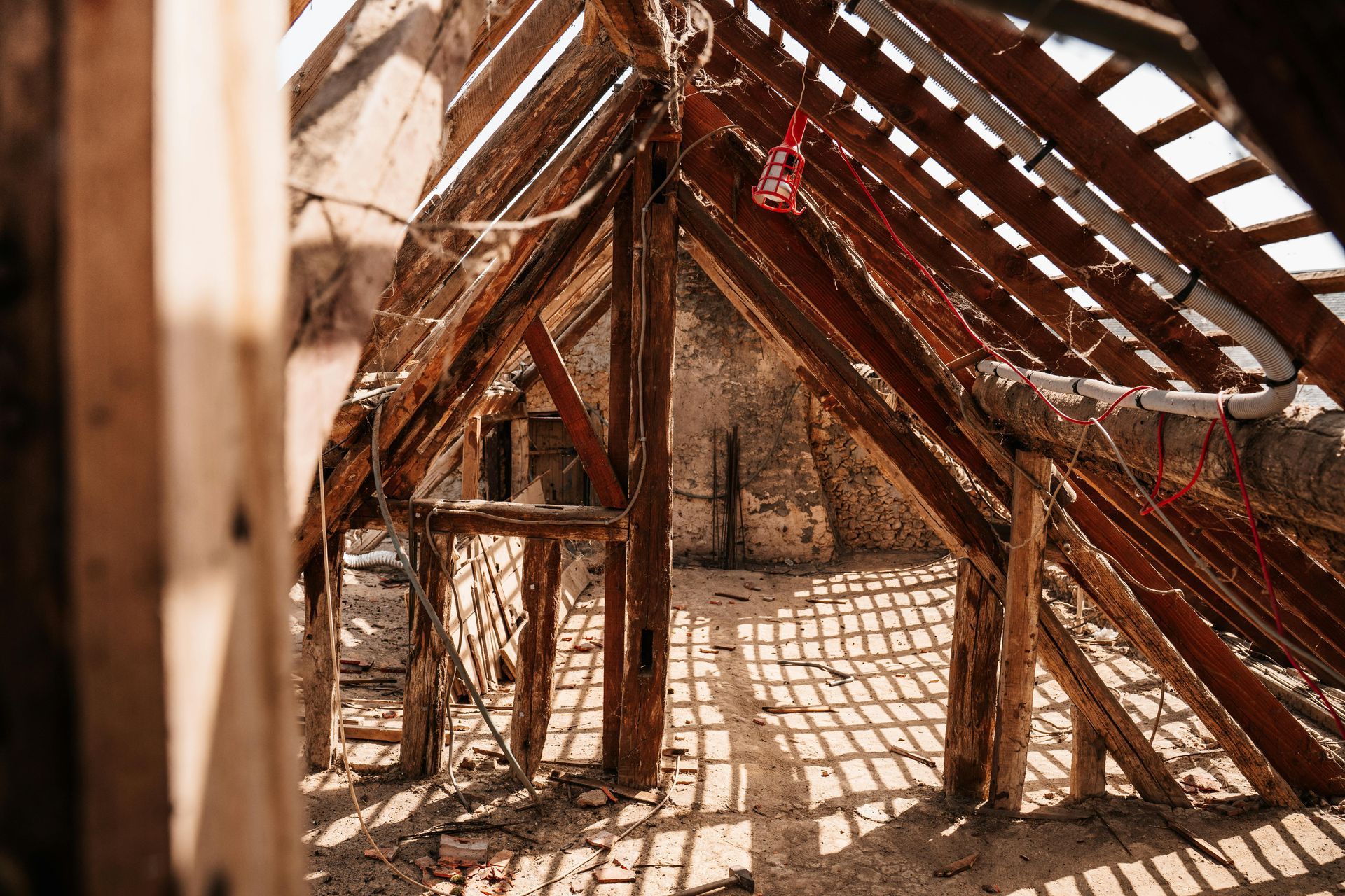 Wooden attic frame with sunlight streaming through the roof, casting shadows on the floor.