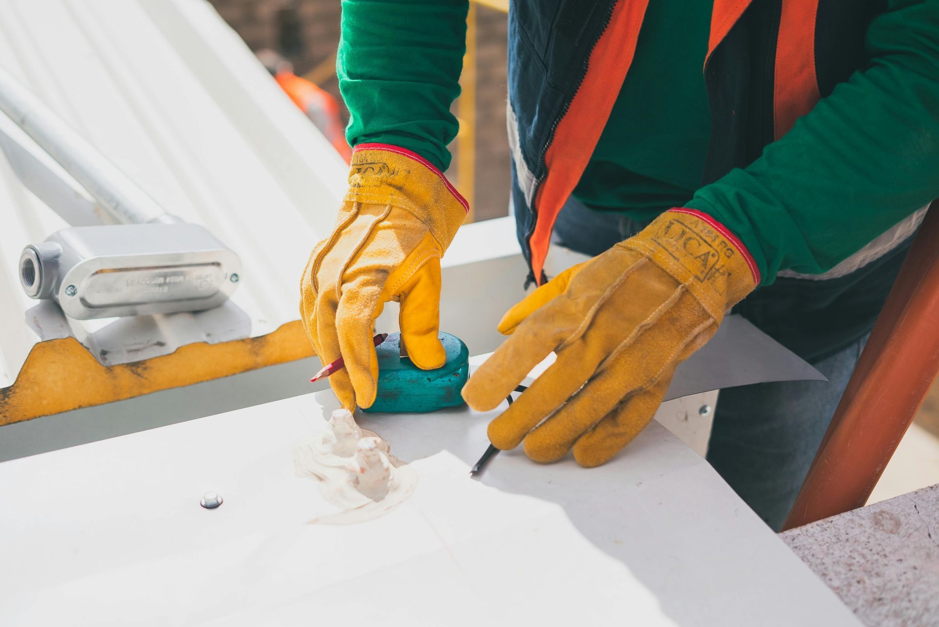 A construction worker wearing gloves is measuring and marking a metal surface.
