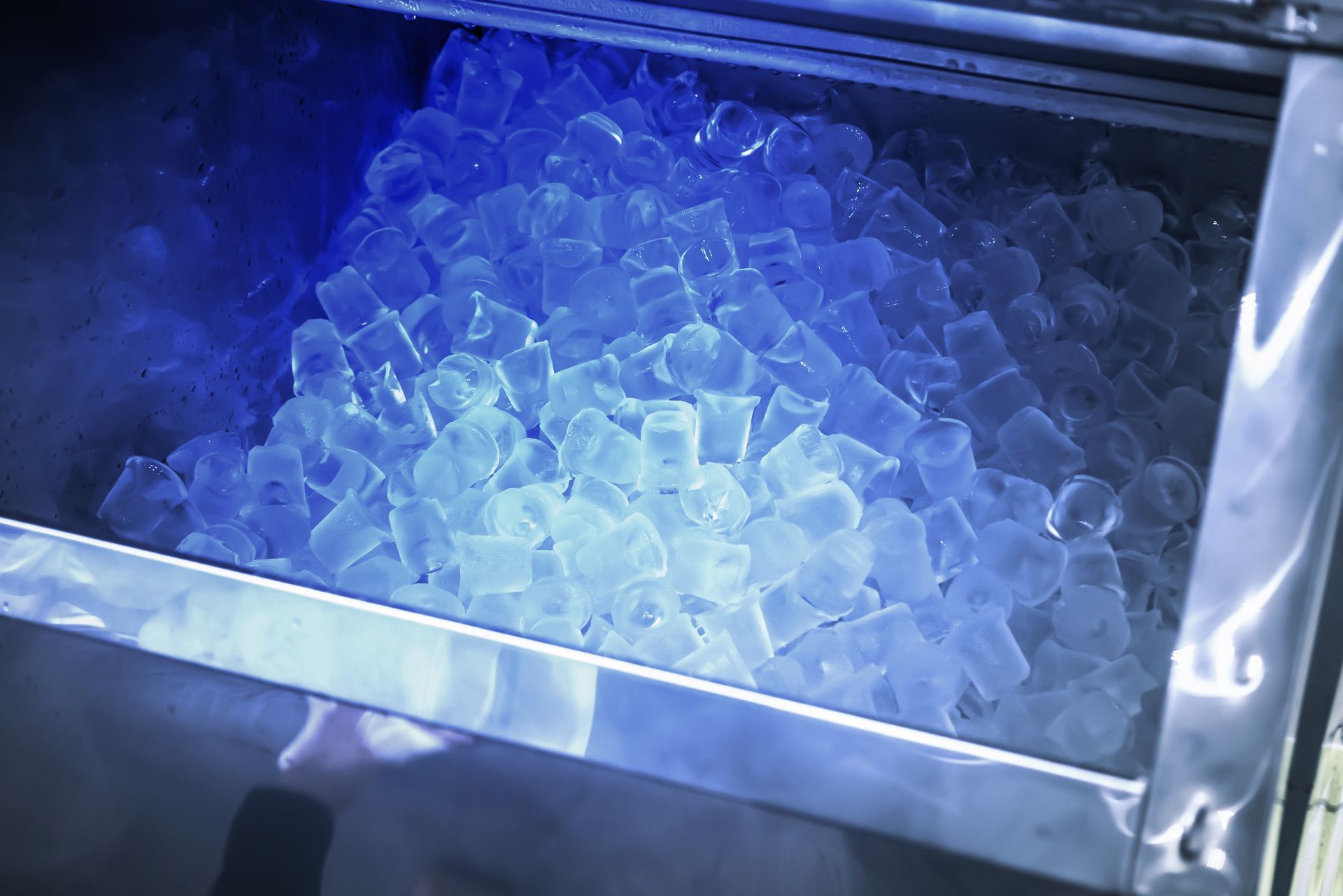A bunch of ice cubes in a container with a blue light shining on them.