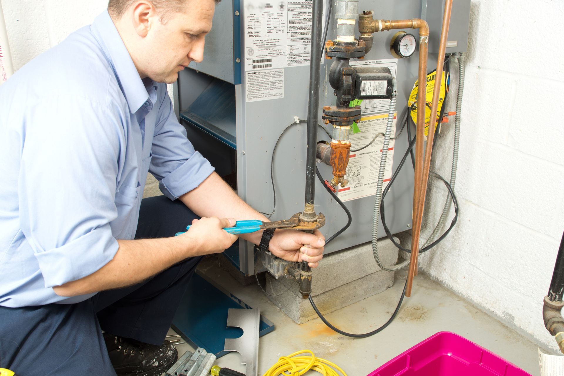 A man is working on a heating system in a basement.