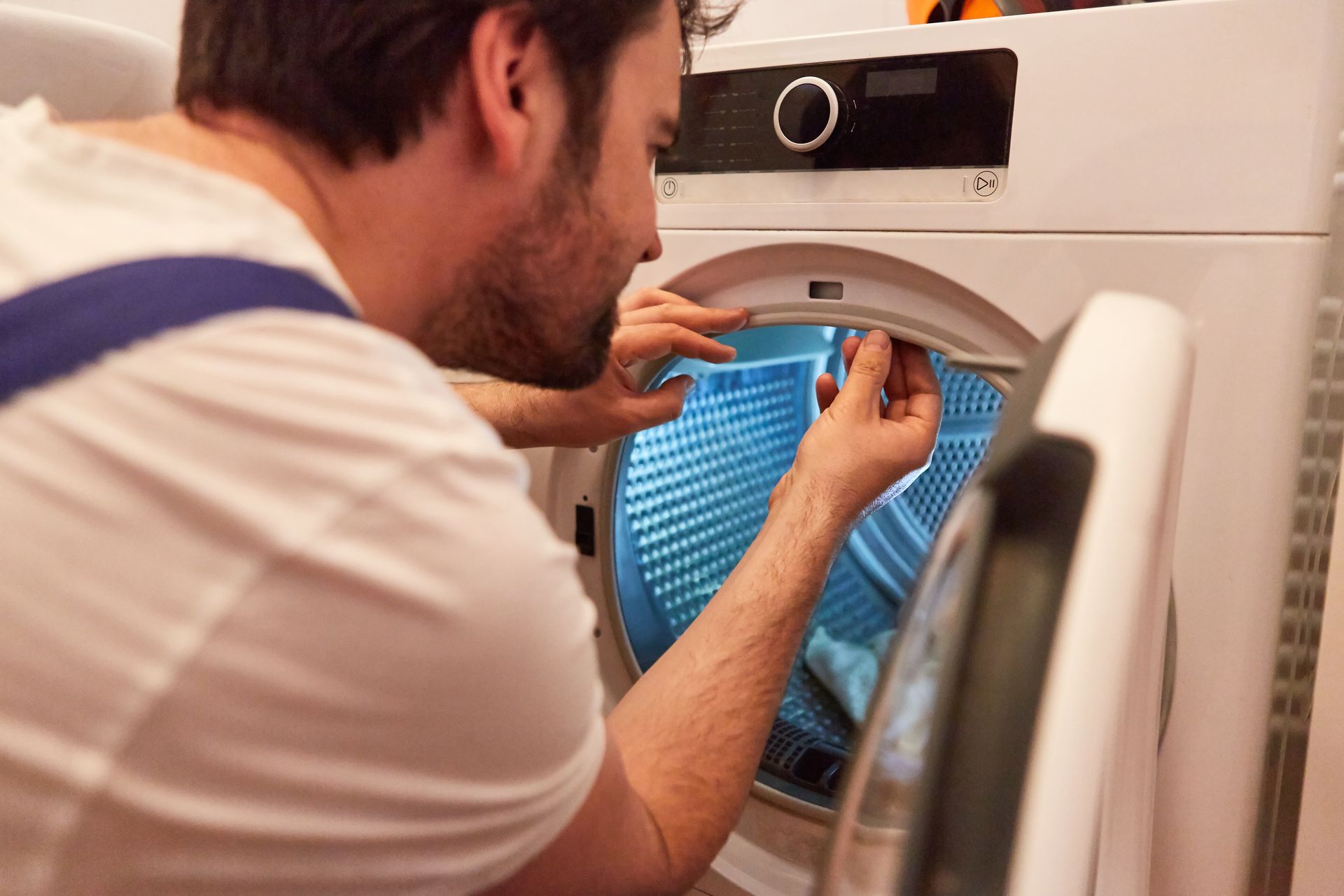 A man is fixing a washing machine in a laundry room.