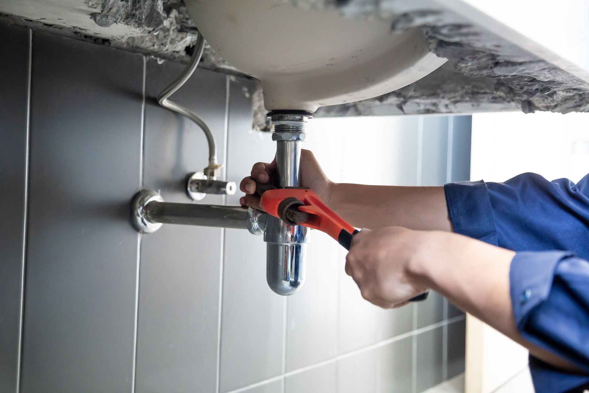 A plumber is fixing a sink with a wrench.
