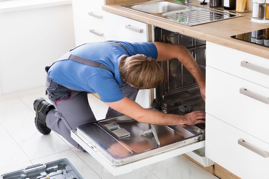 A man is fixing a dishwasher in a kitchen.
