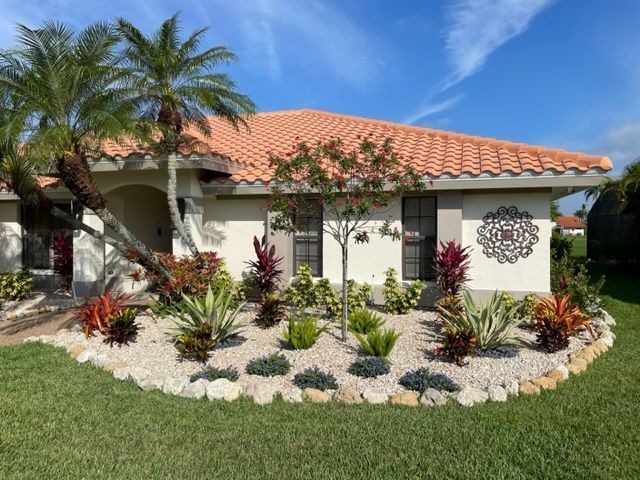 A white house with a red tile roof and a garden in front of it.