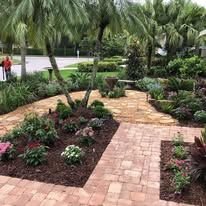 A lush green garden with a brick walkway and lots of plants.