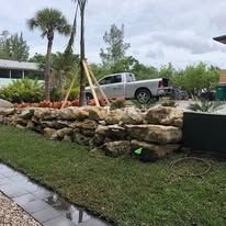 A truck is parked in the grass next to a rock wall.