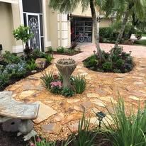 A stone walkway surrounded by plants and trees in front of a house.