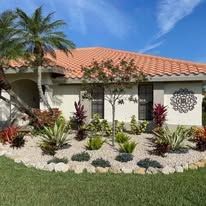 A white house with a red tile roof and a garden in front of it.