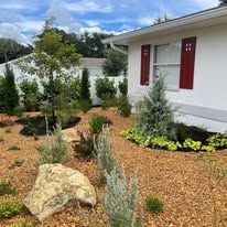 A white house with red shutters and a garden in front of it.