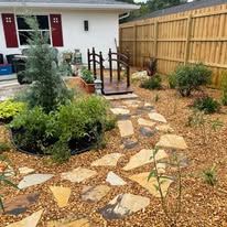 A garden with a wooden fence and a stone walkway leading to a house.