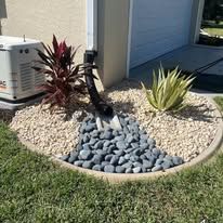 A garden with rocks , plants and a generator in front of a house.