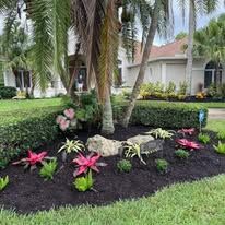 A lush green lawn with flowers and trees in front of a house.