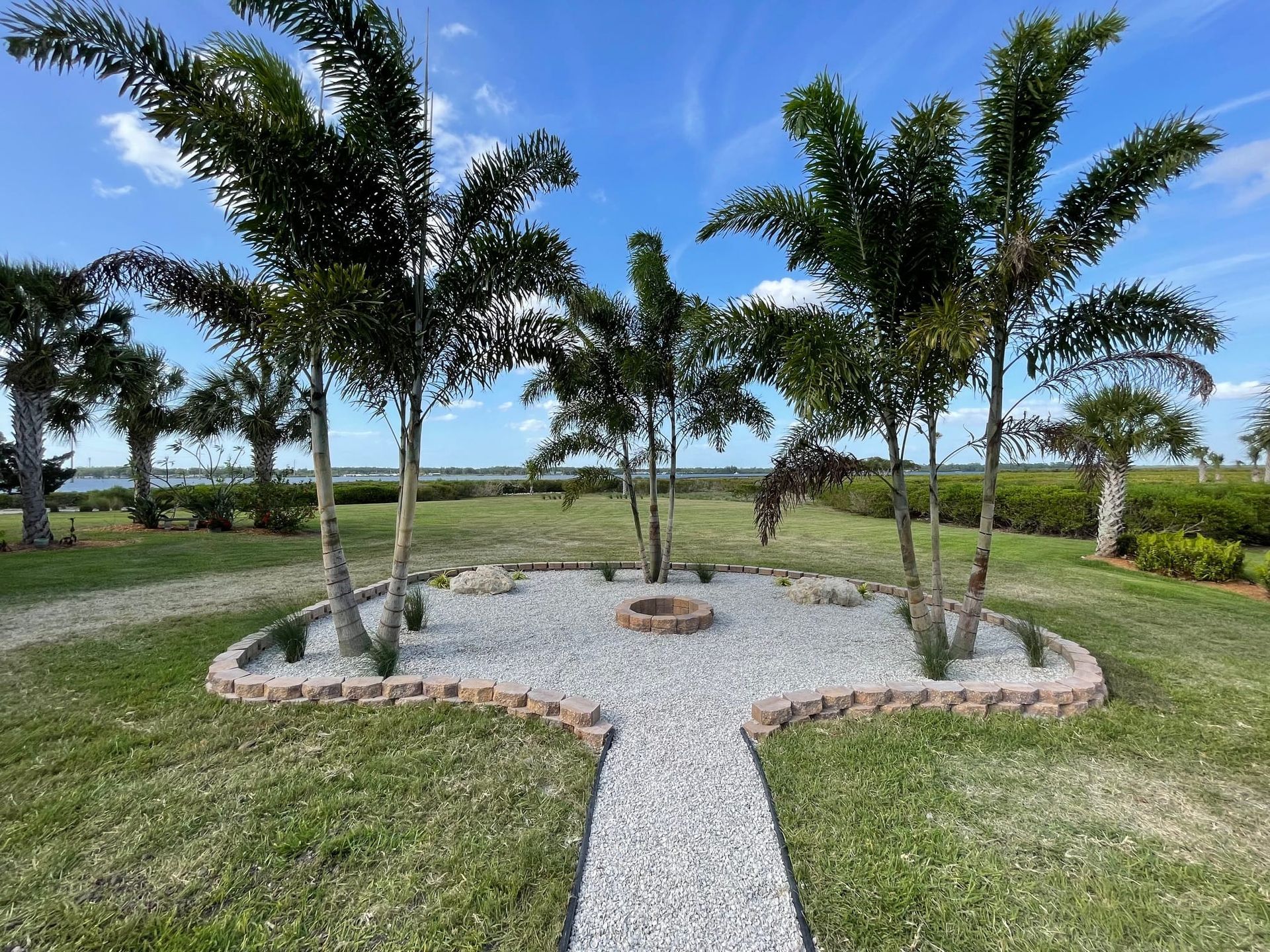 There is a fire pit in the middle of the yard surrounded by palm trees.