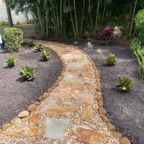 A stone walkway in a garden surrounded by plants and trees.