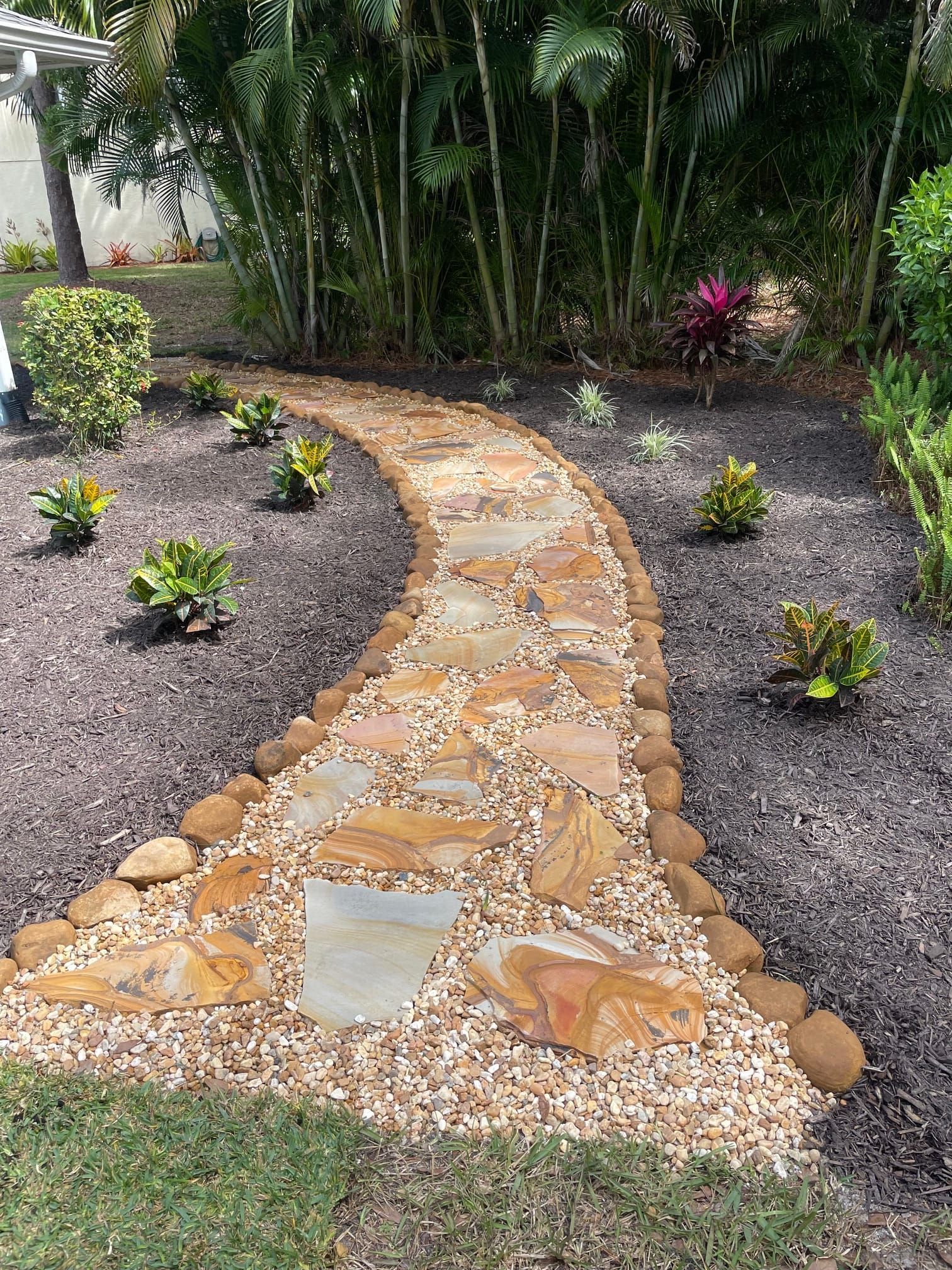A stone walkway in a garden surrounded by trees and bushes.