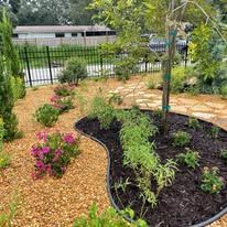 A garden filled with lots of plants and flowers with a fence in the background.