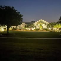 A large house is lit up at night with trees in front of it.