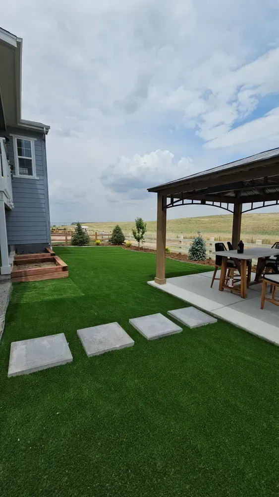 Green lawn with stepping stones leading to a patio with a pergola and outdoor furniture.
