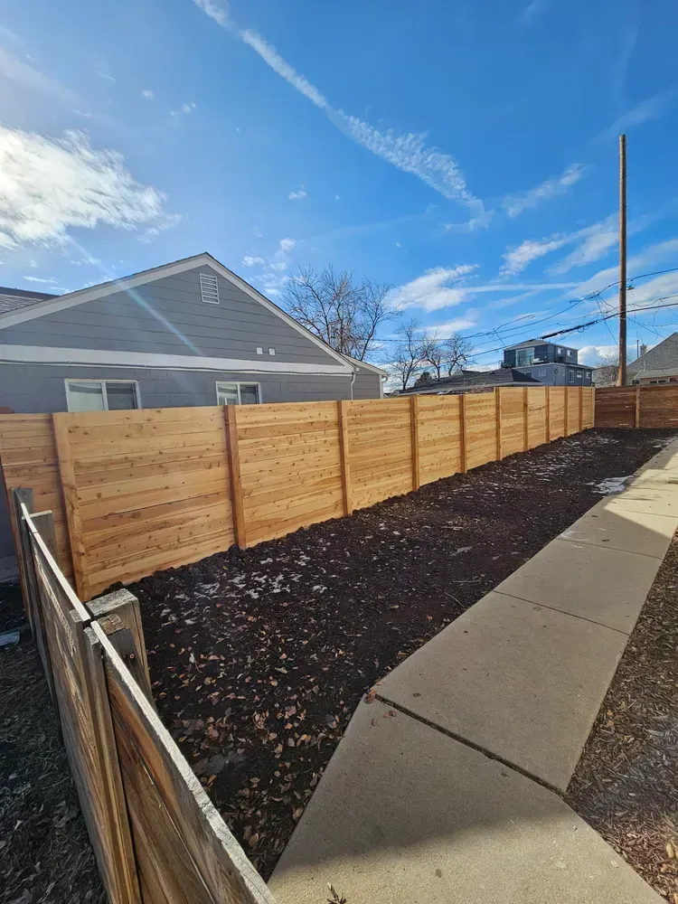 Wooden fence along a sidewalk, separating a yard from the street. 