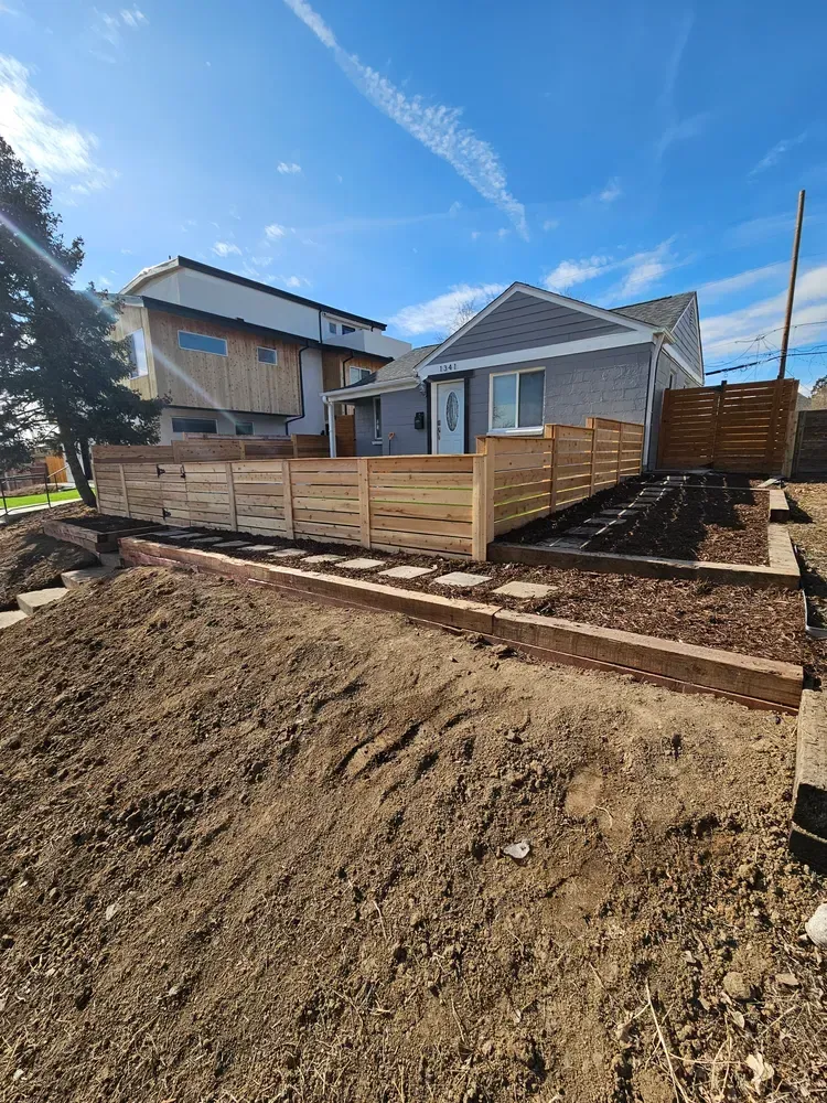A house with a newly constructed wooden fence and landscaping under a blue sky.