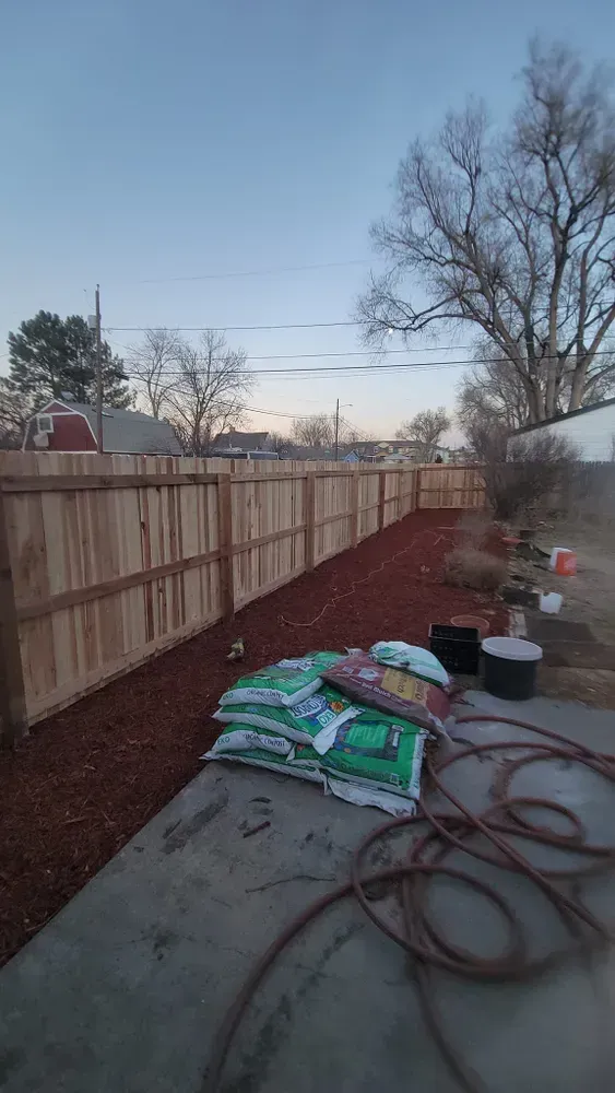 Backyard with a wooden fence, mulch, and bags of soil. 