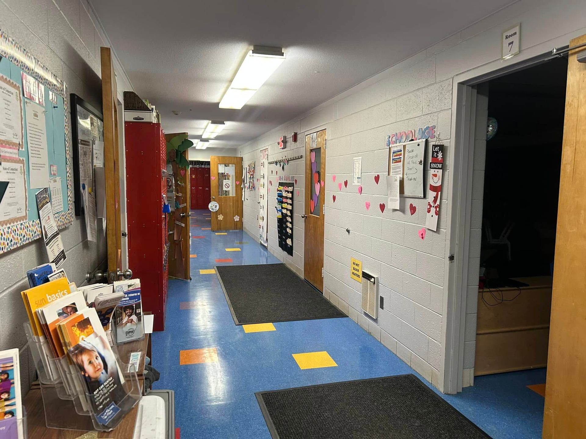 A long hallway with blue floors and a bulletin board on the wall.