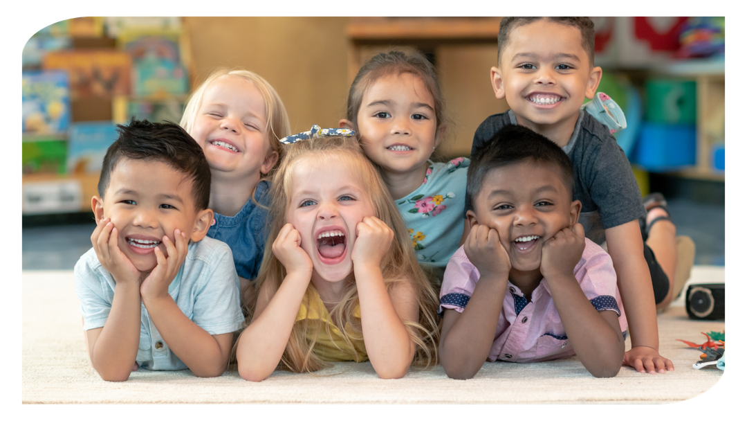 A group of children are laying on the floor and smiling for the camera.