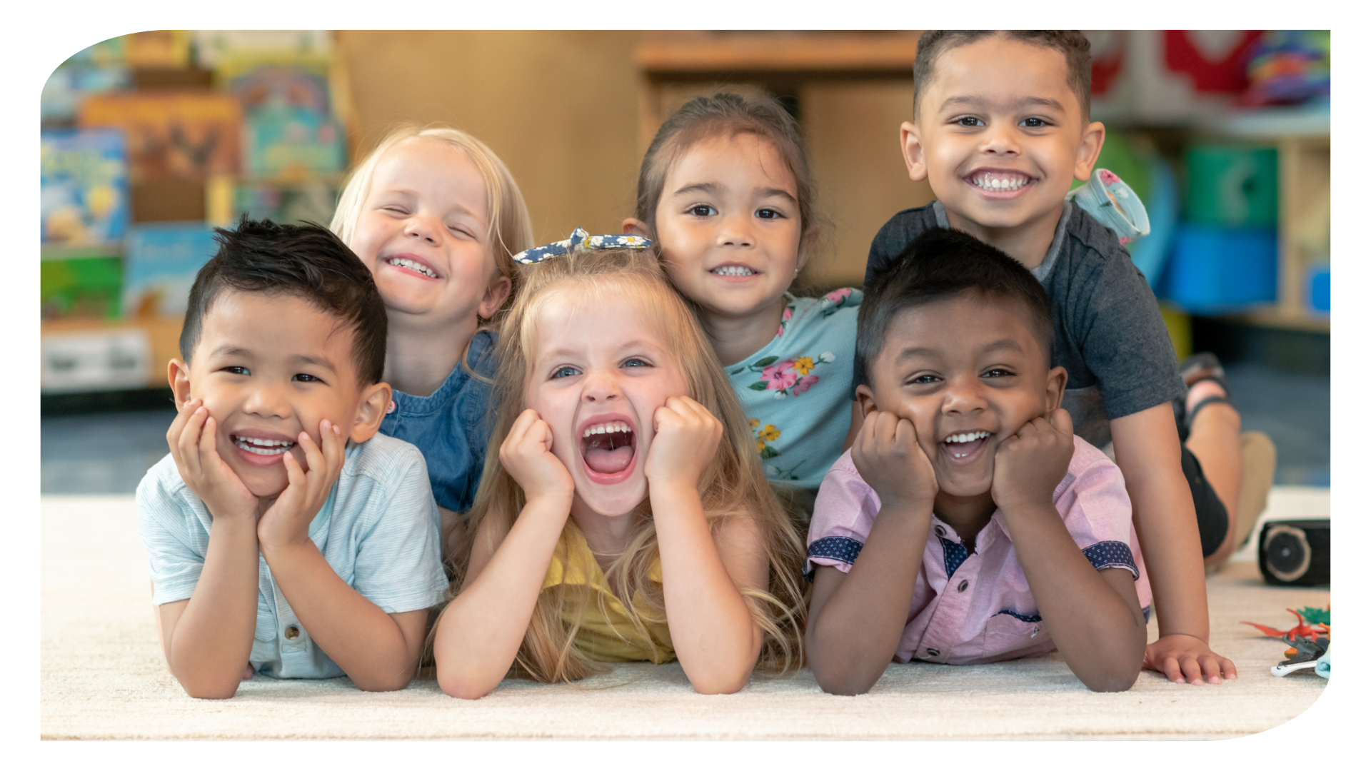 A group of children are laying on the floor and smiling for the camera.