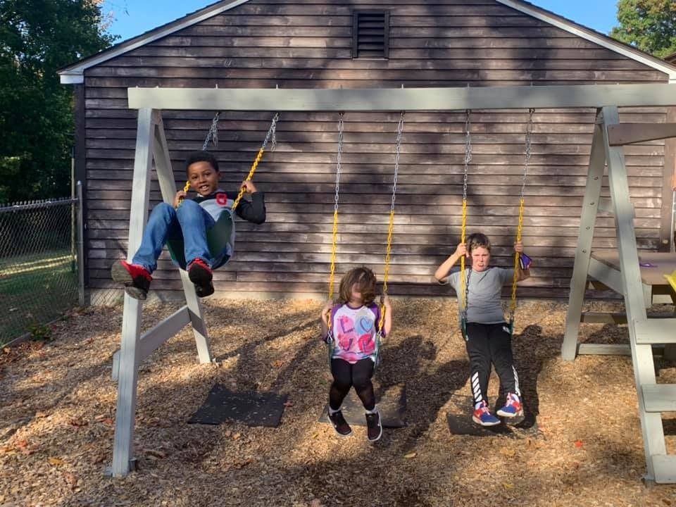 Three children are playing on a swing set in front of a house.