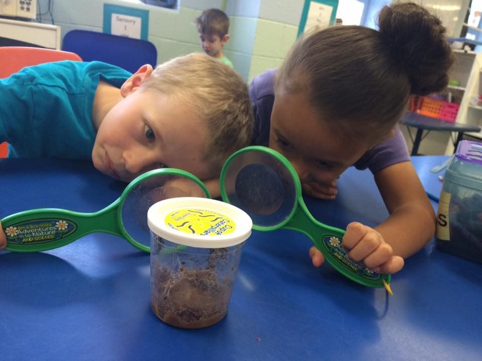 A boy and a girl are looking at a jar with magnifying glasses