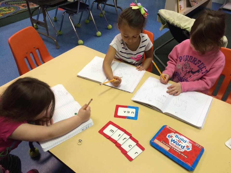 Three young girls are sitting at a table writing in notebooks