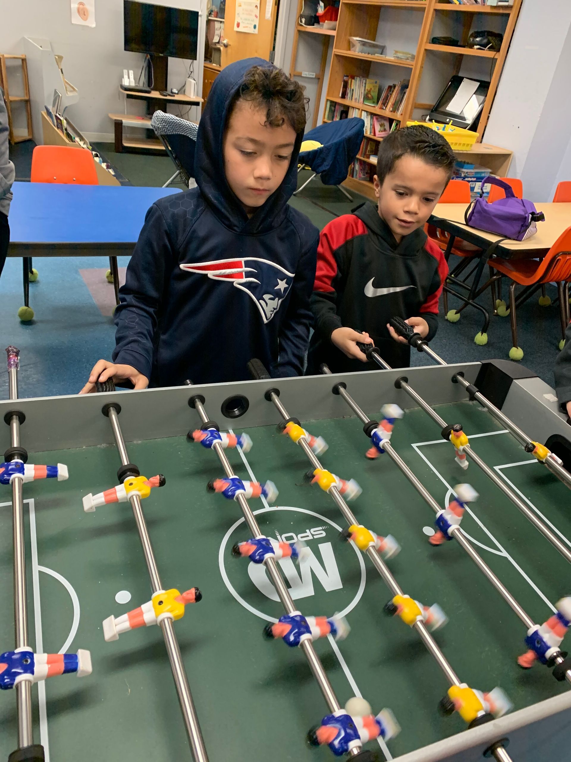 Two young boys are playing a foosball game in a classroom