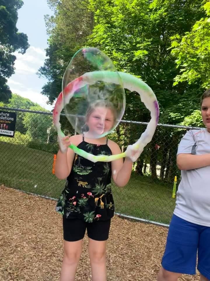 A boy and a girl are playing with soap bubbles in a park.