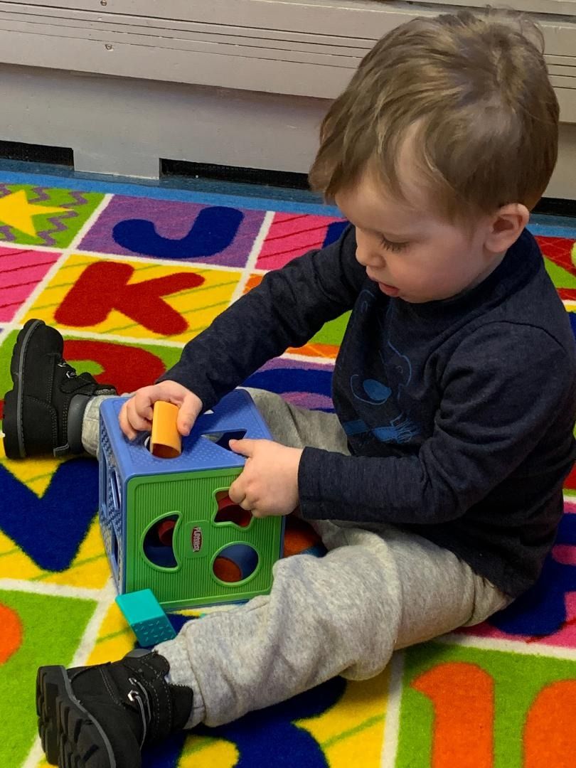 A young boy is sitting on a colorful rug playing with toys