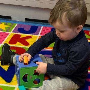 A young boy is playing with a toy on a rug with the letter k on it