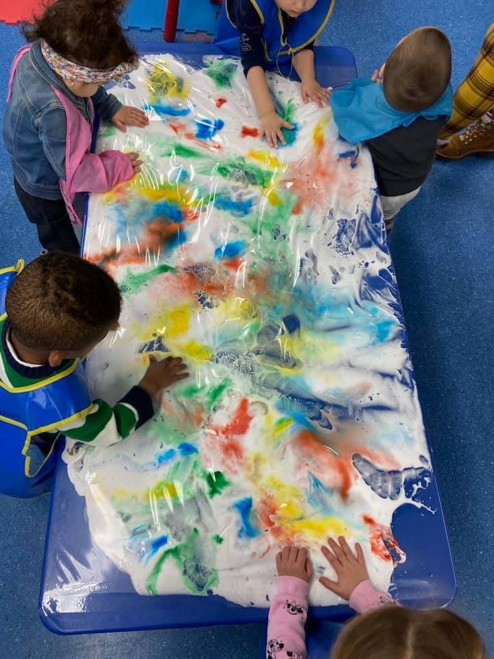 A group of children are playing with foam paint on a table