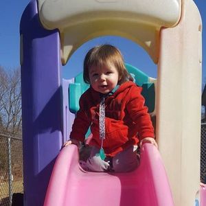 A little girl in a red jacket is sitting on a pink slide