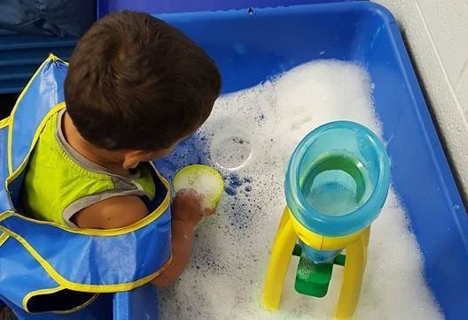 A young boy is playing in a foamy sandbox.