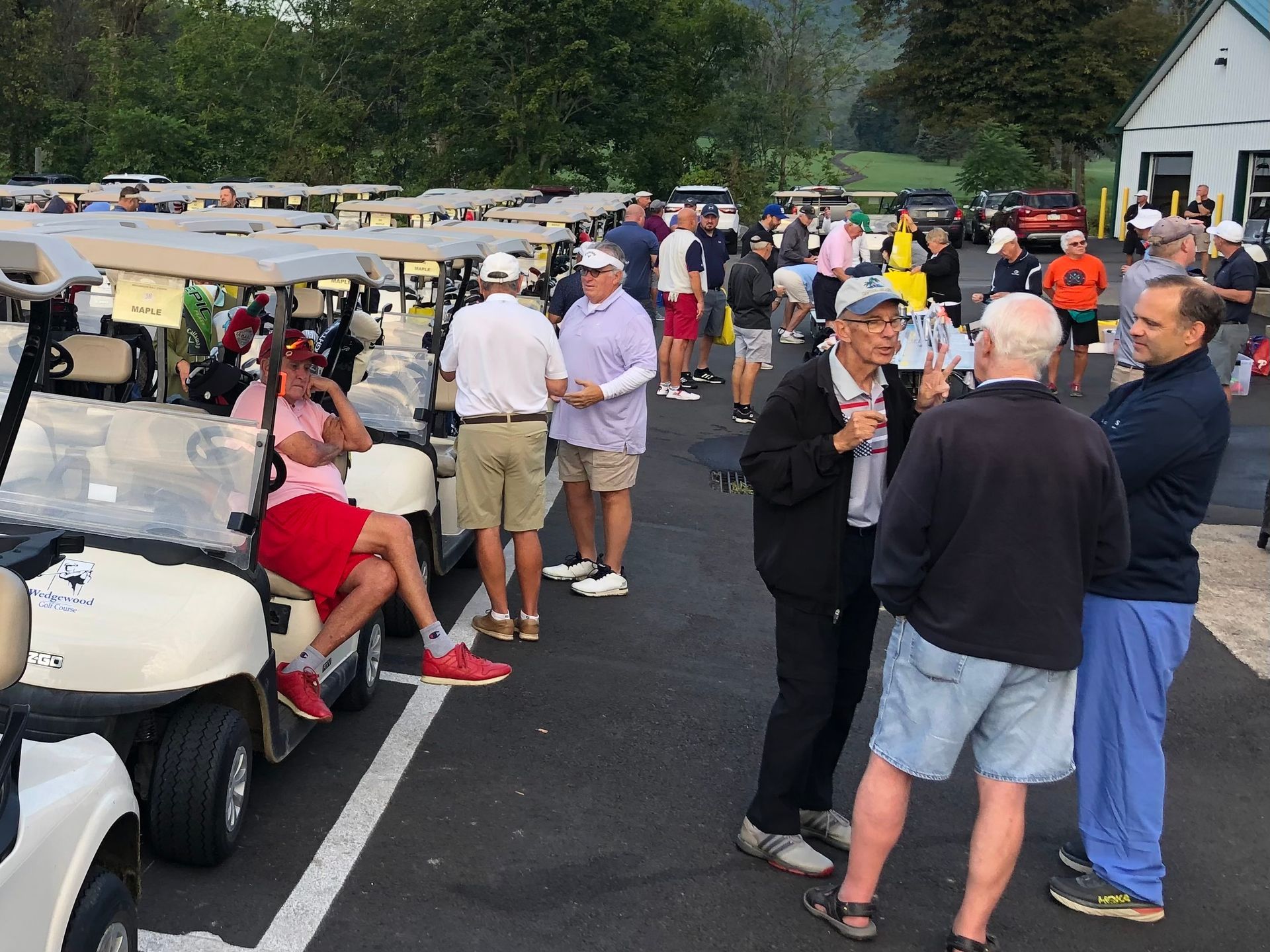 A group of people are standing around golf carts in a parking lot