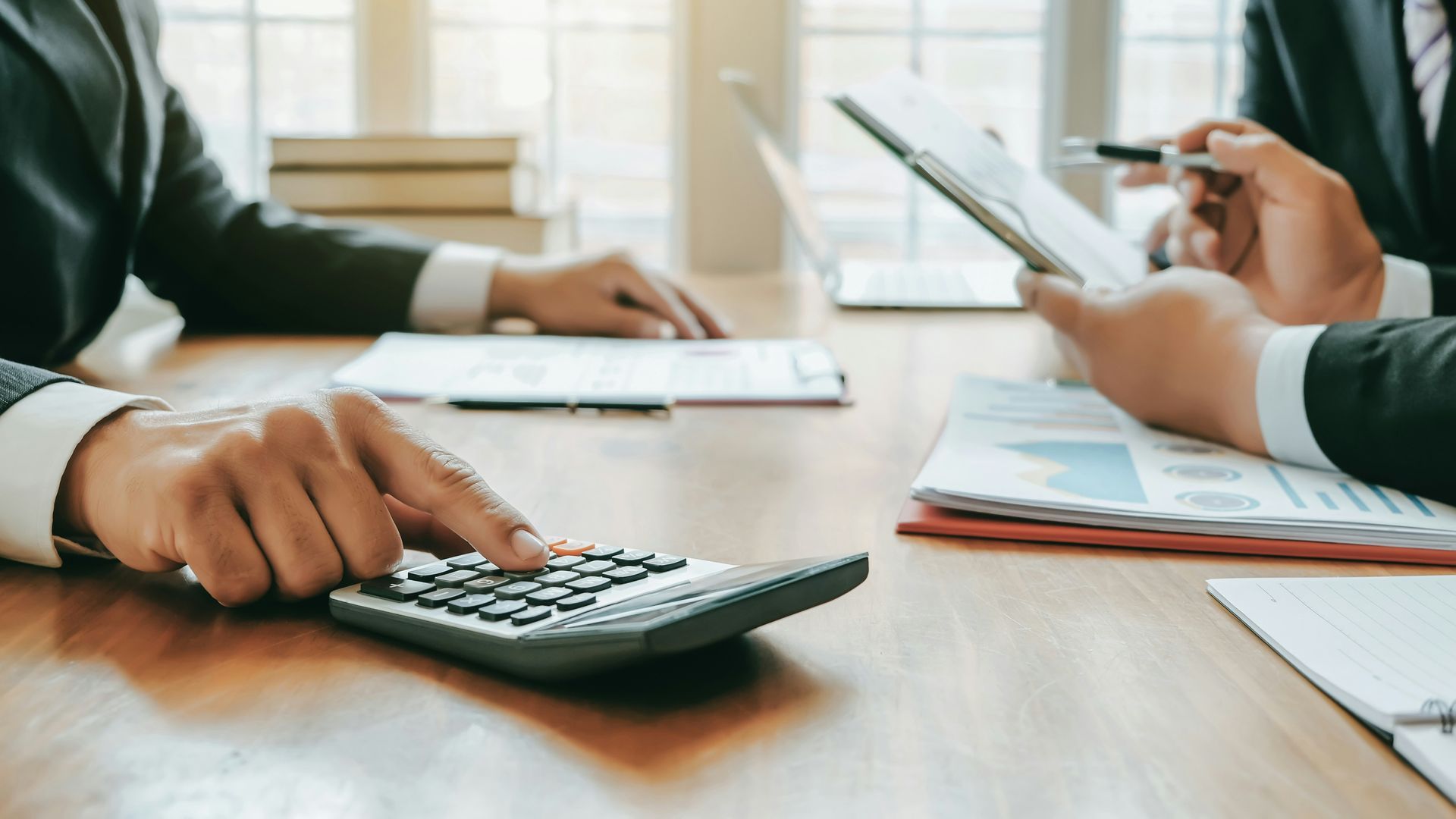 A man is using a calculator while a woman is holding a clipboard.