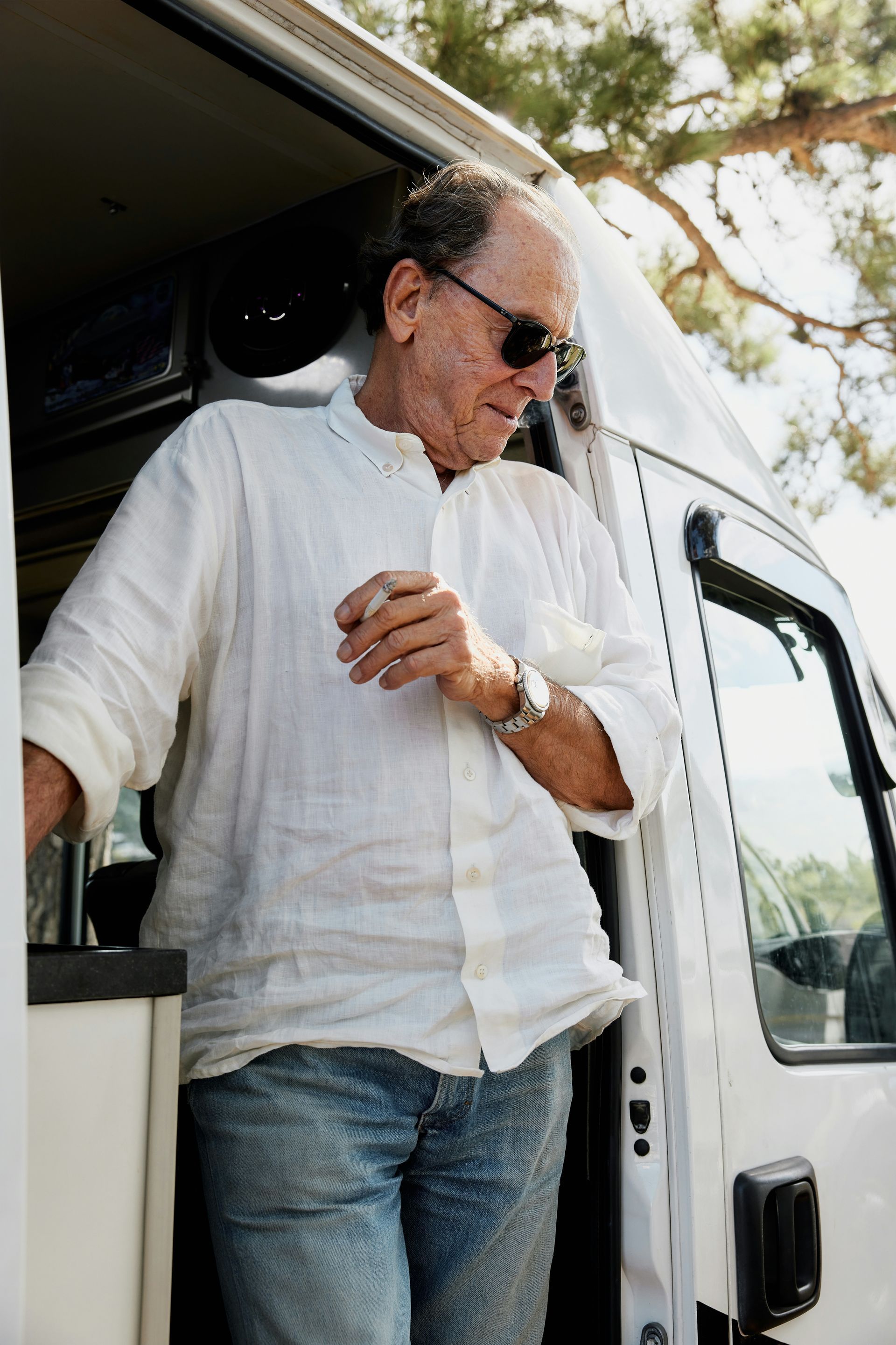 A man wearing sunglasses and a white shirt is standing next to a white van.