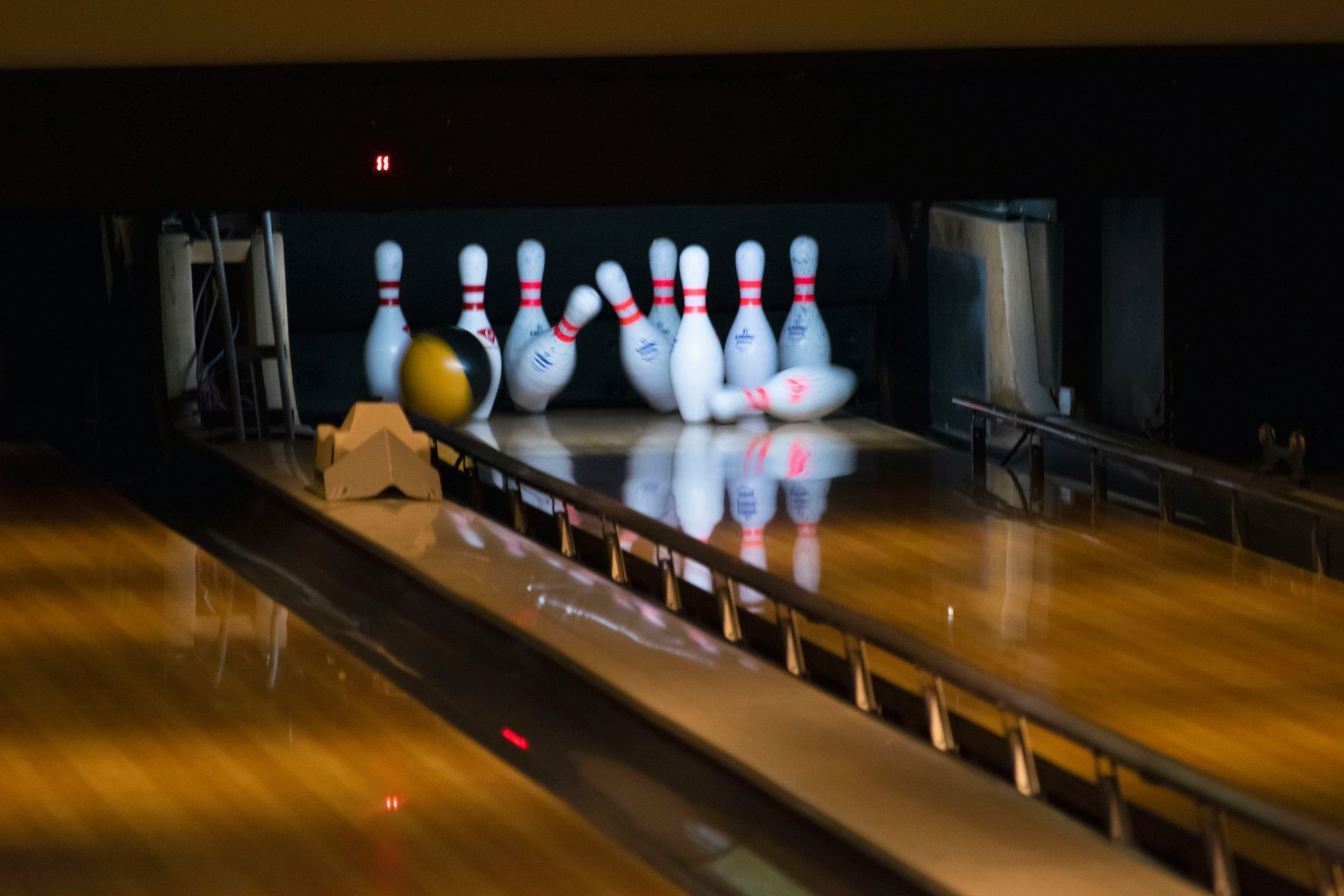 A bowling ball hits pins on a polished lane, with some pins knocked over and others still standing upright.