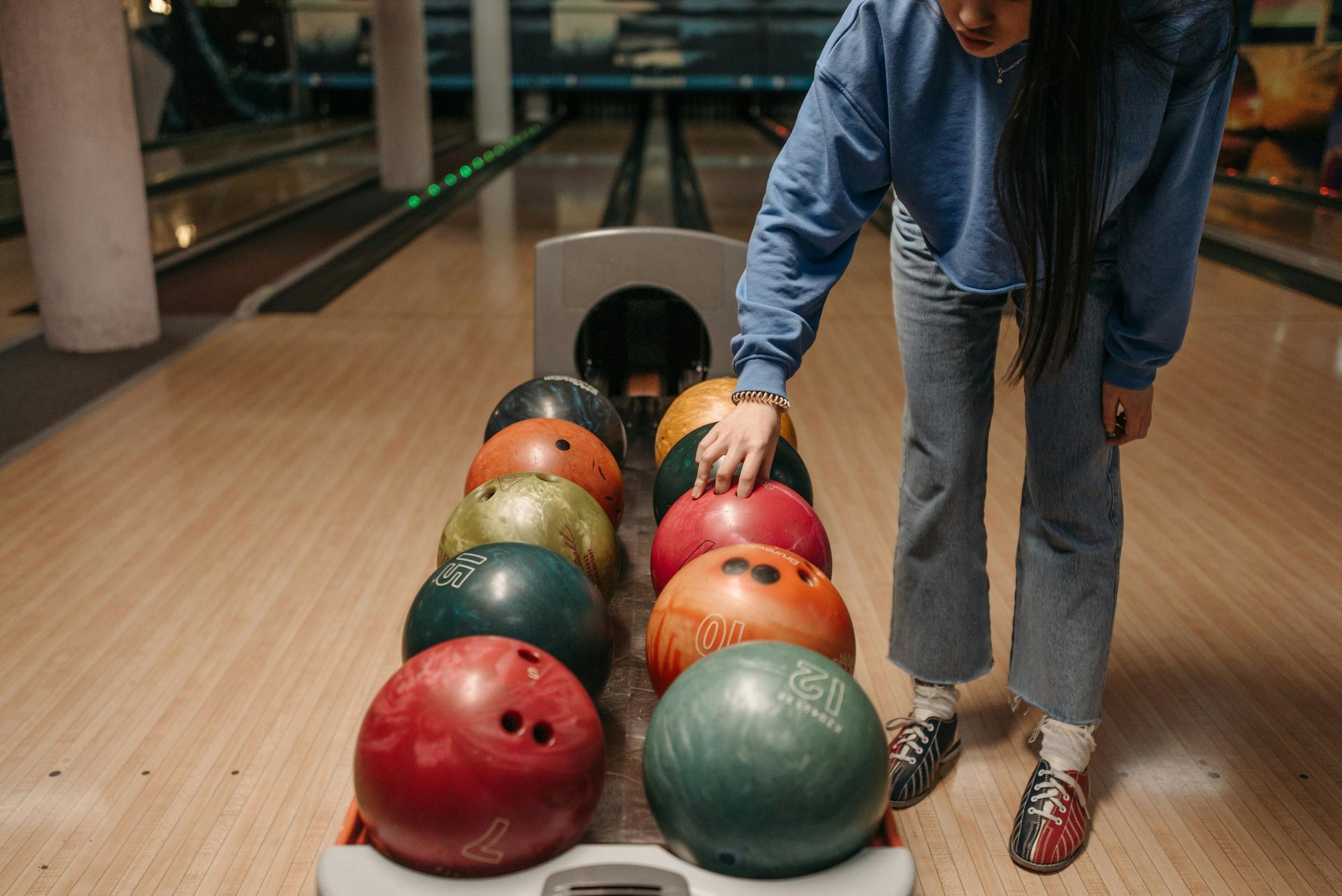 Person choosing a bowling ball. Bowling alley setting. Various colored bowling balls.