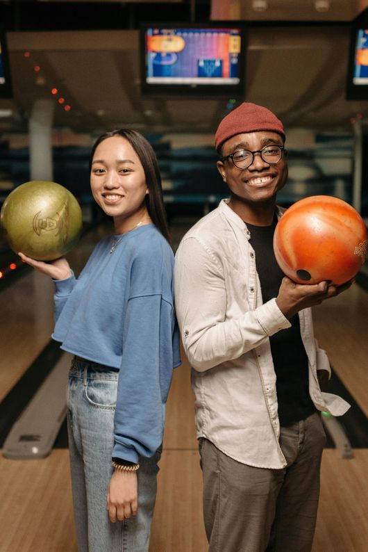 A man and a woman are standing back to back holding bowling balls.