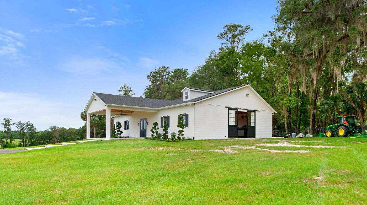 A white house is sitting on top of a lush green field next to a tractor.